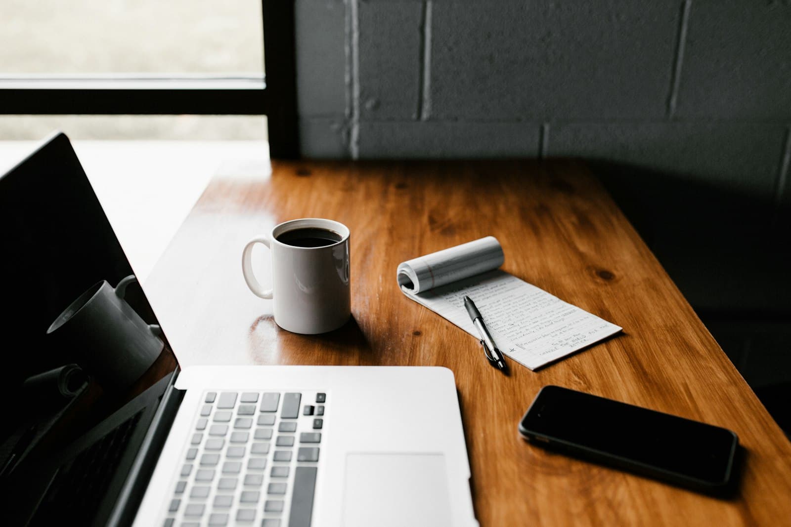 A notebook and laptop on a desk beside a cup of coffee