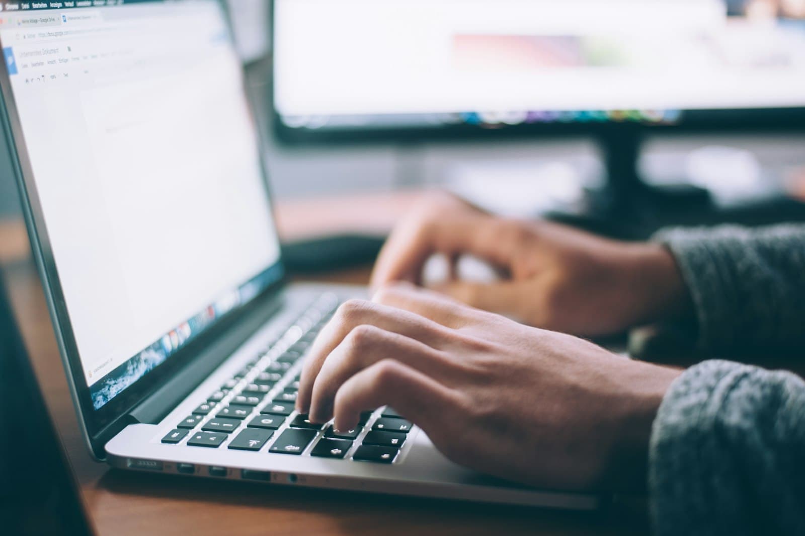 Someone typing on a laptop at a wooden table